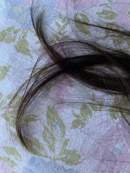 Long brown hair on cotton sheets with a pastel floral pattern in natural light.