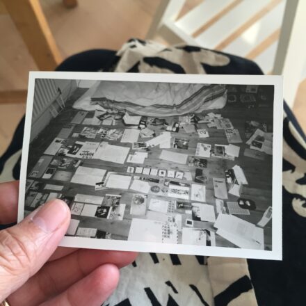 A photo of a hand holding a black and white of letters laid carefully out on a wooden floor in a flat in Hulme Manchester